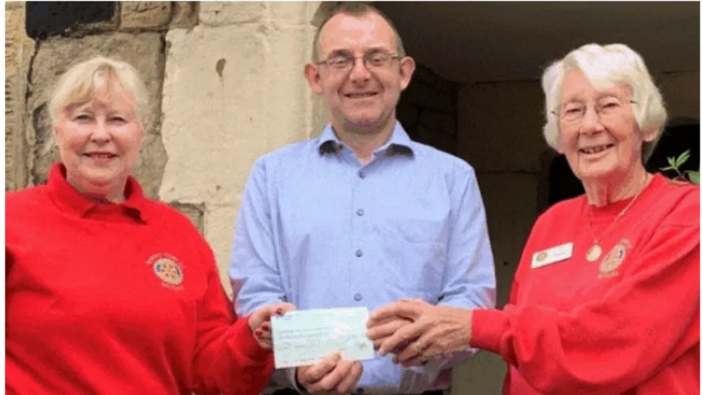 Image of two women dressed in red presenting a cheque to Tom Taylor - our previous Chief Executive