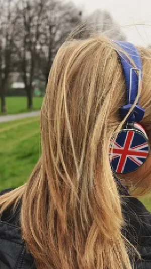 Photo of a women with long hair. She has union jack headphones on and is walking in the countryside. She is facing away from the camera.