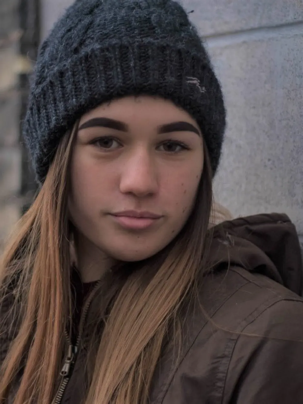 Photo of a young woman with long hair. She's wearing a grey woolly hat.