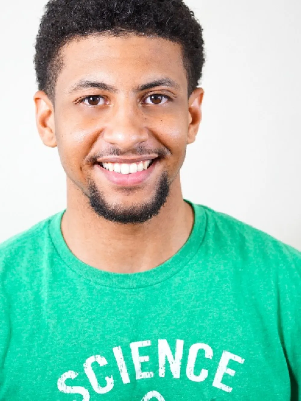 Photo of young man with beard smiling broadly, He's wearing a green shirt.