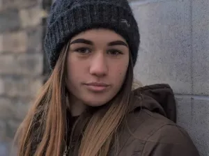 Photo of a young woman with long hair. She's wearing a grey woolly hat.