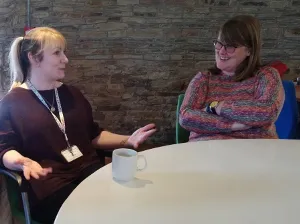 Two white women seated at a round table chatting and drinking tea.