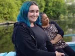 Photo of a young woman with blue hair. There is another woman behind her. They are on a boat.