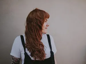 Image of young woman with long brown hair. She's wearing dungarees.