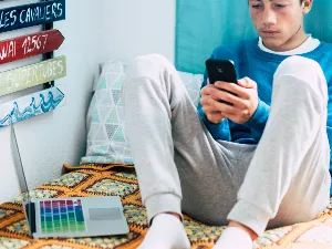 teenage boy sitting on bed looking at stuff on his mobile.