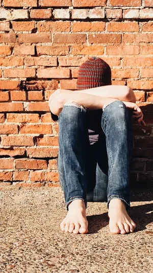 Photo of a young person with their head in their arms - seated against a brick wall