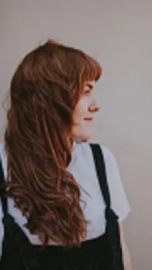 Image of young woman with long brown hair. She's wearing dungarees.