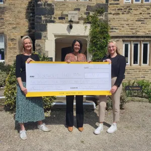 PHOTO OF 3 PEOPLE HOLDING A LARGE CHEQUE IN FRONT OF THE HALL